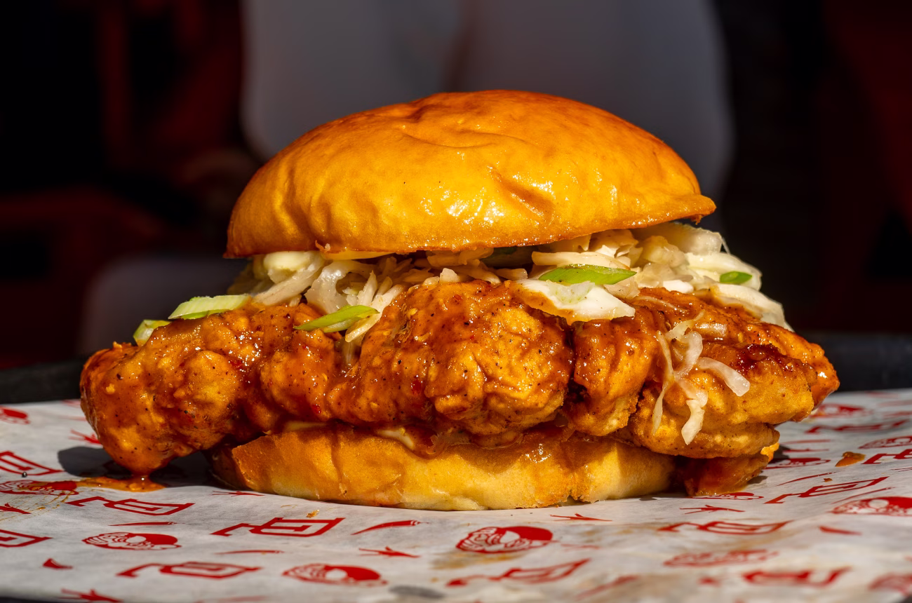 A fried chicken sandwich with coleslaw, scallions and spicy dipped chicken.